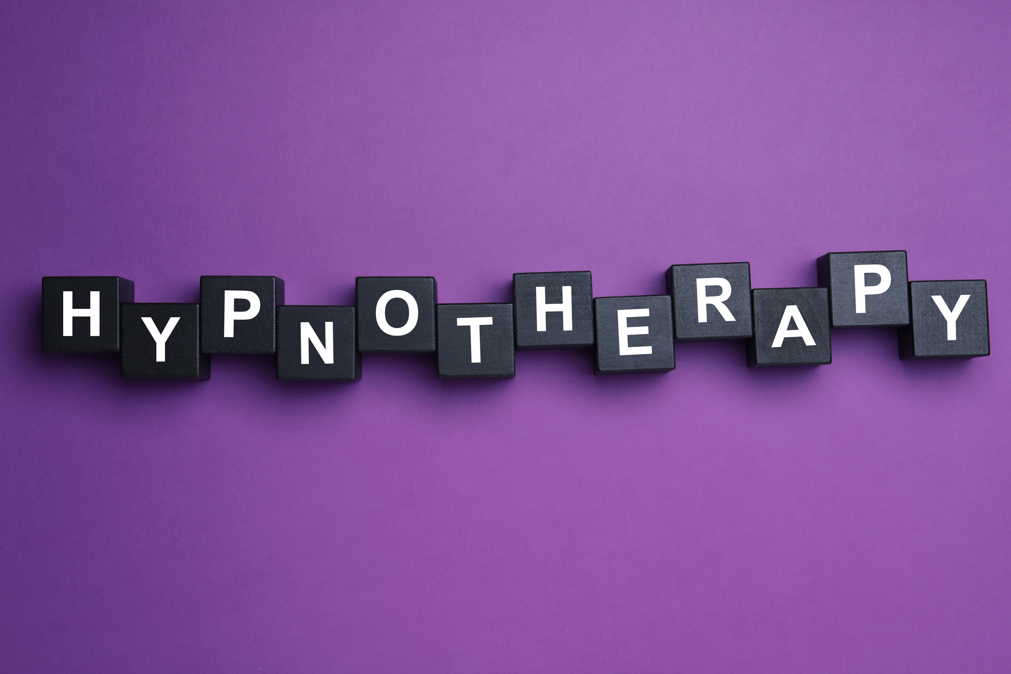 Black Wooden Blocks with Word HYPNOTHERAPY on Purple Background,